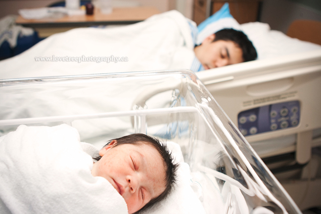 a father and newborn sleep side by side in the hospital. a must have picture for any new family; image by www.lovetreephotography.ca